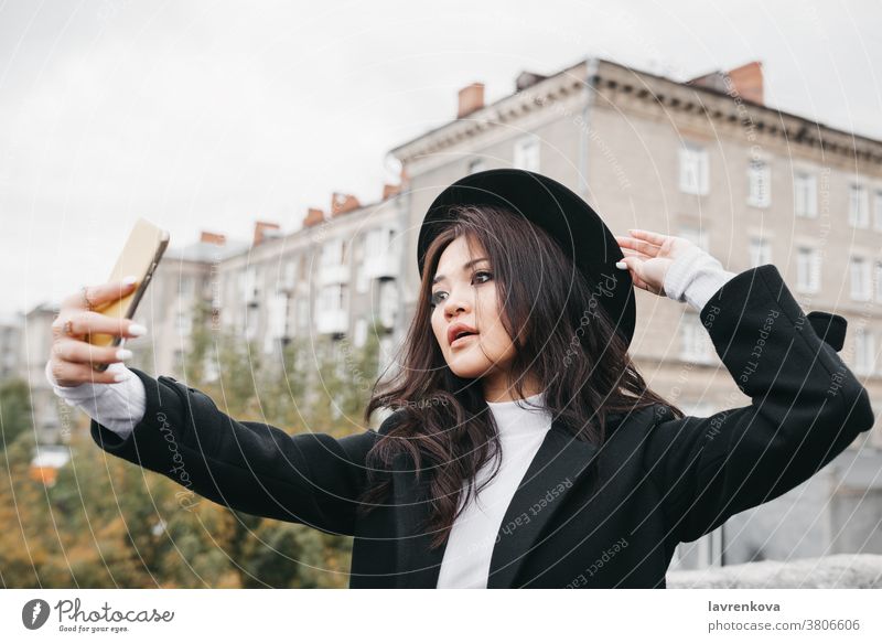 Junge Asiatin in dunklem Mantel und Hut, die im Freien ein Selfie macht asiatisch Mobile Foto Frau Dame Fotokamera Smartphone Mädchen Lifestyle jung Spaß Bild