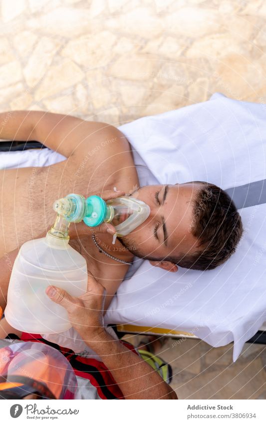 Patient mit Sauerstoffmaske am Meeresufer im Sommer Rettungsschwimmer geduldig Mundschutz Unterstützung Mitarbeiterin Hilfsbereitschaft COVID vertieft Strand