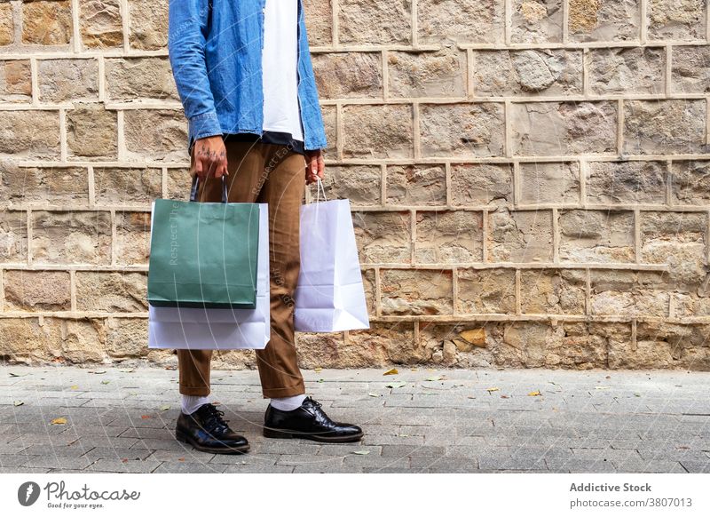 Crop stilvolle Shopaholic mit Einkaufstaschen auf der Straße konsumgeil stylisch Bekleidung umweltfreundlich Vorschein Stilrichtung Mann Straßenbelag Wand Öko