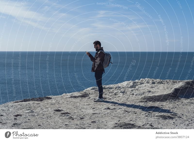 Junge männliche Tourist erholsam auf Klippe Rand gegen blaue Meer Mann sich[Akk] entspannen MEER benutzend Smartphone Erholung bewundern Reise Reisender Saum