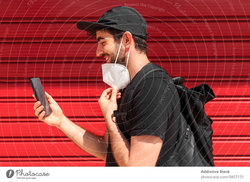 Mann mit Maske führt Videoanruf auf Smartphone Video-Chat Freundin Bildschirm Partnerschaft Lächeln Mundschutz Bund 19 benutzend Apparatur Wand sprechen