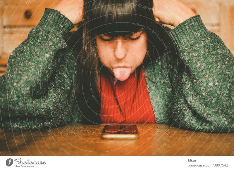 Eine junge Frau ist genervt und streckt  ihrem Smartphone die Zunge raus. Genervt wütend Handy Technik Digitalisierung Online Dating Mobbing trotzing online