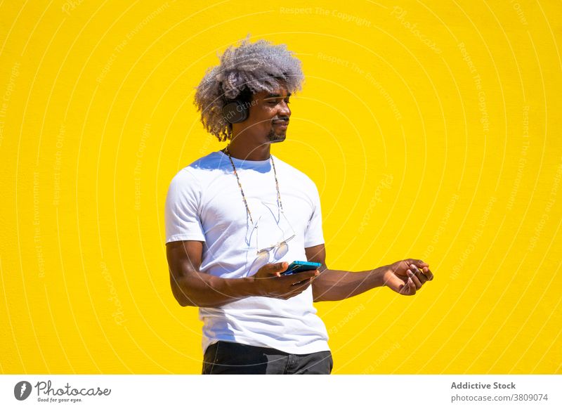 Schwarzer Mann mit Afro-Haar hören Musik mit Kopfhörer und Musik hören Tanzen Afrohaar Tanzlehrer schwarz gelber Hintergrund Afro-Look zuhören lässig Straße
