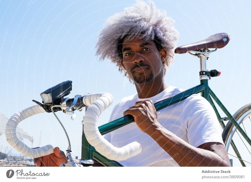 Afro und schwarzer Mann, der ein Stadtrad auf seinem Rücken trägt. Schwarzer Fahrer Tragen des Fahrrads Tragen eines Fahrrads Reiter Schwarzer Reiter tragen