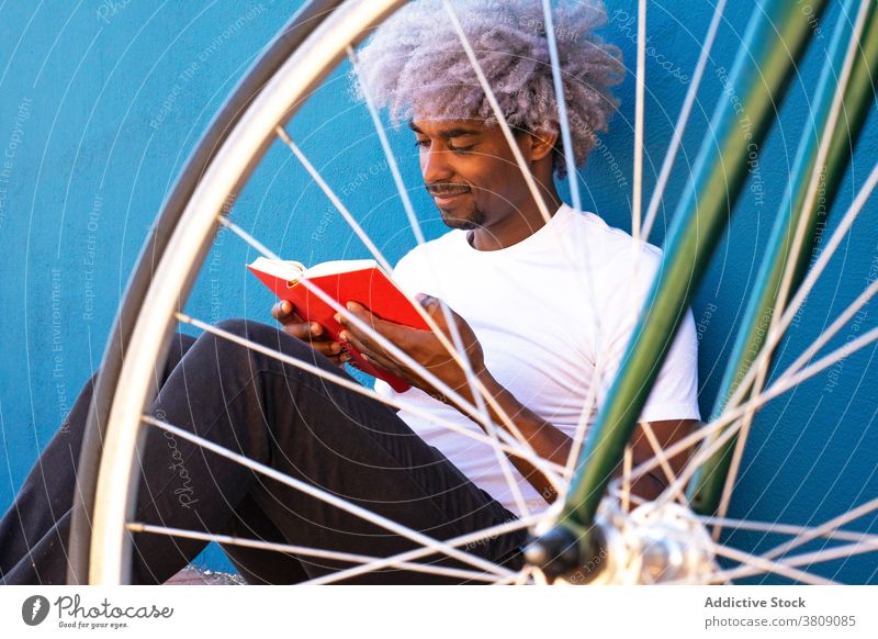 Schwarz und afro Mann liest ein Buch neben seinem Fahrrad. Konzept o lesen Schwarzer Mann liest Lesen eines Buches Rotes Buch Afro-Mann Afro schwarzer Mann