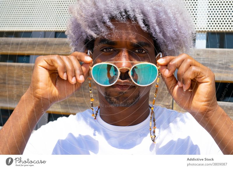 Schwarzer Mann mit Afro-Haar, der eine Sonnenbrille aufsetzt. Sonnenbrille und ein Afrohaar Afro-Look schwarz Sonnenbrille aufsetzen Afrikanisch Afro-Mann Stil