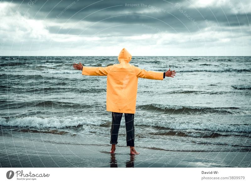 Mann im Friesennerz steht mit ausgebreiteten Armen am Meer Ozean umarmen Unwetter Wellen Ferien & Urlaub & Reisen Wasser Küste Wolken stürmisch gigantisch weite