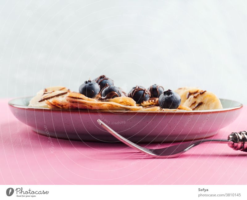 Crêpes mit Schokolade und Heidelbeeren essen Banane Haselnuss Gabel Kronleuchter rosa süß Frühstück Nahaufnahme Aufstrich Maslenitsa serviert Pfannkuchen