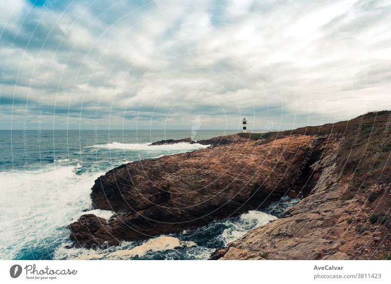 Ein wilder Leuchtturm an der Küste im Norden Spaniens mit riesigen Felsen und wilden Wellen, die mit Kopierraum krachen winken Schifffahrt Anleitung Dämmerung