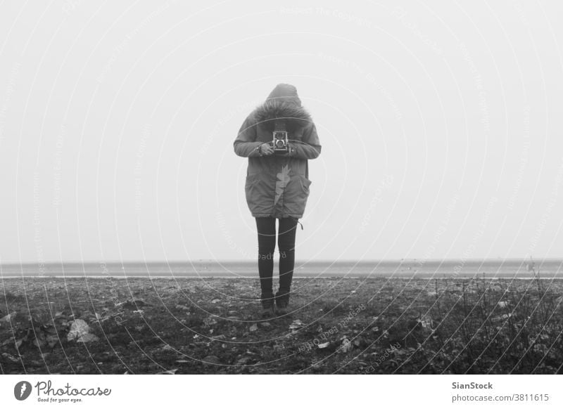 Frau mit Retro-Kamera in einer Nebel-Landschaft Fotokamera neblig schwarz weiß SCHWARZ-WEIß altehrwürdig Winter Kunst retro Mädchen unter Person Fotograf