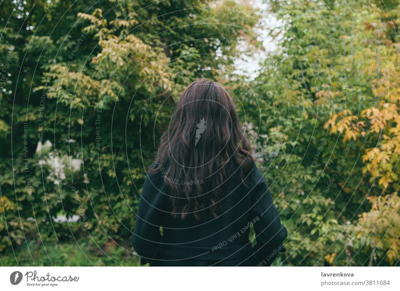 Porträt vom Rücken eines Weibchens in dunklem Mantel im Freien im Park oder Wald allein kalt Frau schön Behaarung fallen Bäume Erwachsener Jacke Herbst laufen