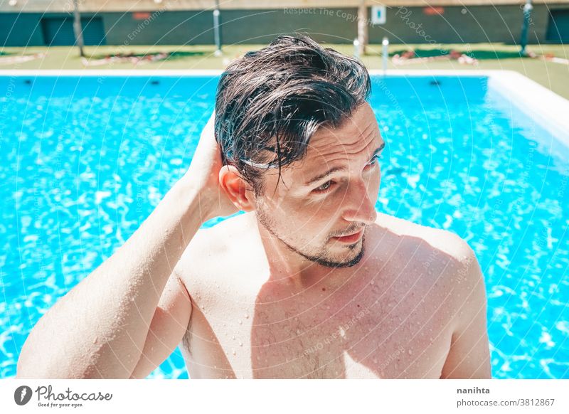 Junger, gutaussehender Mann posiert in der Nähe eines Pools attraktiv sexy männlich Schwimmbad Sommer Haut Vollbart Typ Lächeln Bräune blau Wasser Party Porträt