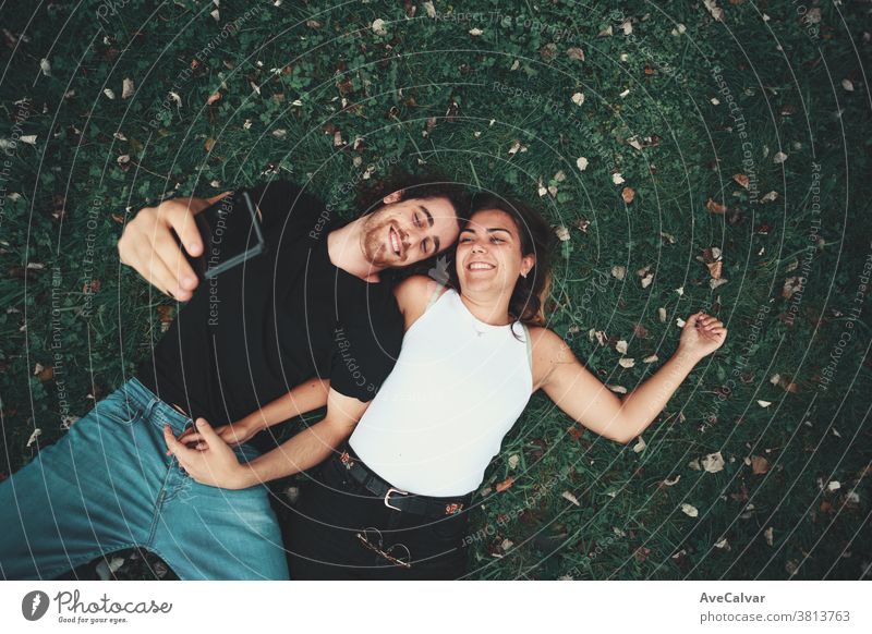 Junges Paar, das sich auf dem Rasen liegend ein Selfie macht Menschen Mann Smartphone Park Porträt Gras klicken Glück niederlegen Technik & Technologie