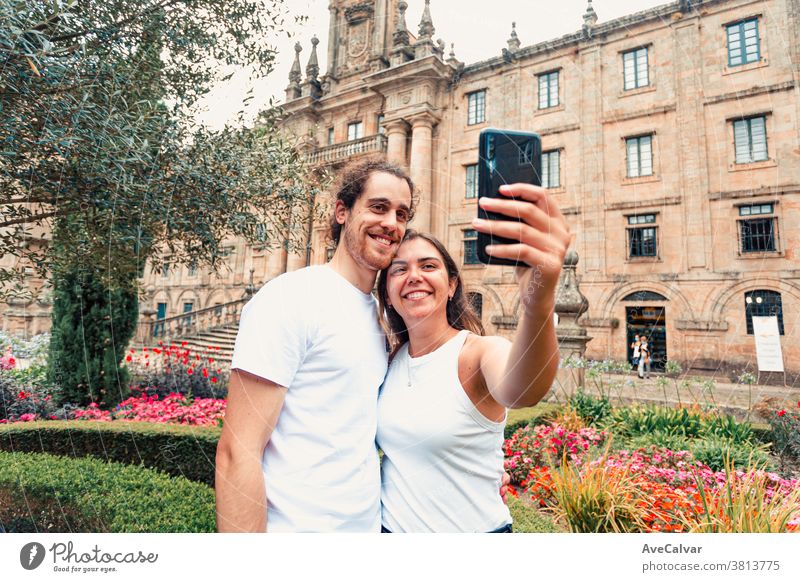 Junges Paar macht sich in einem Garten vor einem alten Gebäude ein schönes Selfie Feiertag Glück Smartphone Urlaub brünett Mann im Freien Küssen Bild männlich