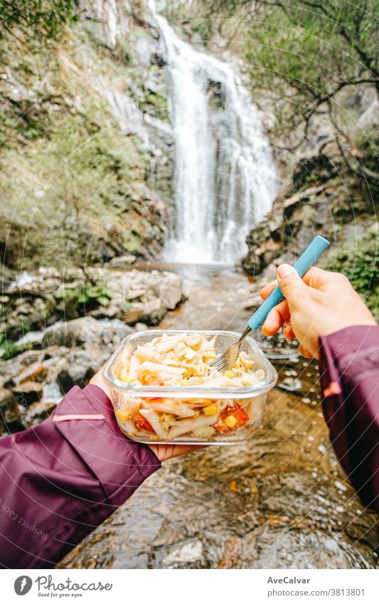 Blickwinkelaufnahme einer Wanderin, die vor einem Wasserfall isst Koch Überleben Picknick gierig Menschen Rucksacktourismus Erholung Menschengruppe Lager Zelt