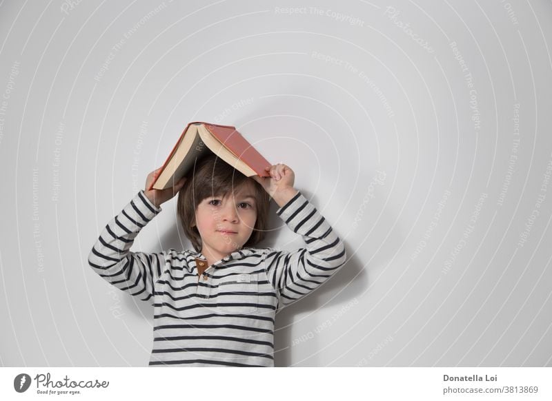 Kinderporträt mit Buch auf dem Kopf bezaubernd Junge Kaukasier heiter Kindheit niedlich Tag Bildung Emotion Ausdruck Gesicht Spaß Fröhlichkeit Glück Beteiligung