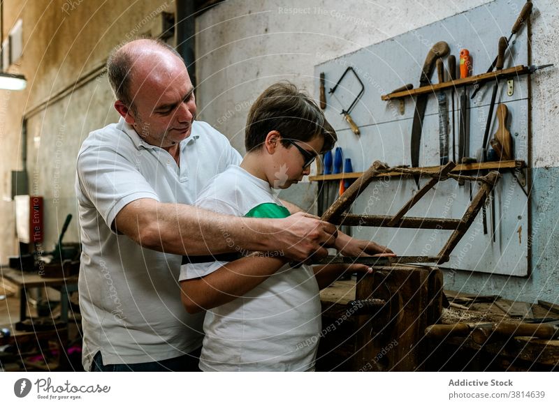 Männlicher Holzarbeiter unterrichtet Sohn in der Werkstatt Holzarbeiten raspeln Vater lehren lernen Metall Werkzeug abstützen schäbig Gerät Prozess Hobby Beruf