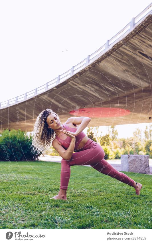 Fokussierte Frau übt Yoga im Park gedrehte Sichellonge parivrtta anjaneyasana Asana beweglich Pose verdrehen üben Gleichgewicht positionieren schlank Wellness