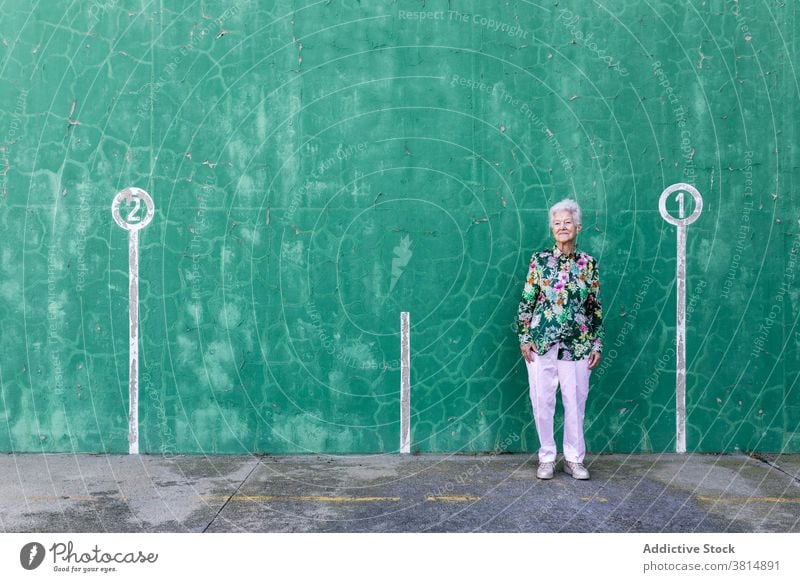 Stilvolle ältere Frau steht in der Nähe der Wand Senior gealtert elegant Outfit selbstbewusst positiv Inhalt graues Haar Lächeln Lifestyle Optimist Erfahrung