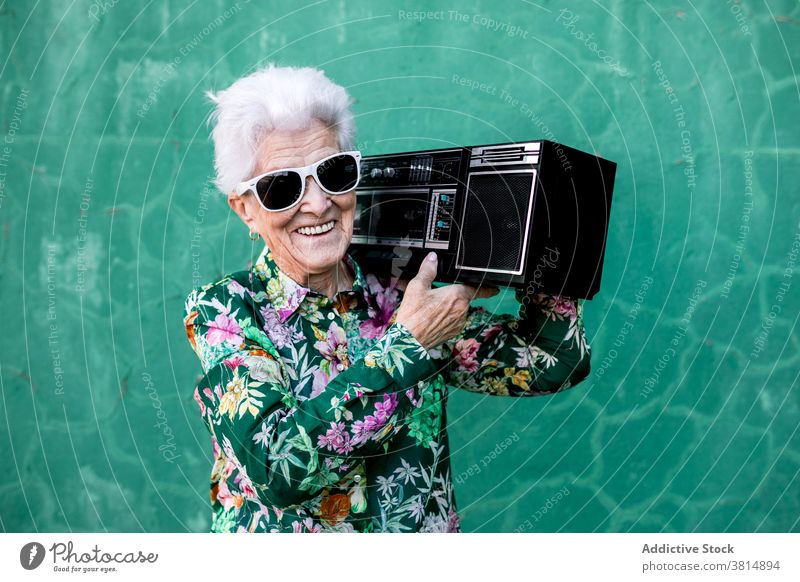 Ältere Frau mit Plattenspieler in der Nähe der Wand stehend Senior Spieler Musik Stil älter zuhören Klang aktiv Aufzeichnen trendy Lifestyle urban gealtert