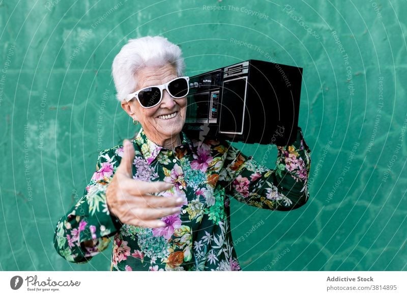 Ältere Frau mit Plattenspieler in der Nähe der Wand stehend Senior Spieler Musik Stil älter zuhören Klang aktiv Aufzeichnen trendy Lifestyle urban gealtert