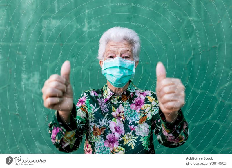 Ältere Frau in medizinischer Maske zeigt Daumen hoch Senior Mundschutz Coronavirus Optimist positiv behüten gestikulieren Bund 19 COVID19 Pandemie älter Zeichen