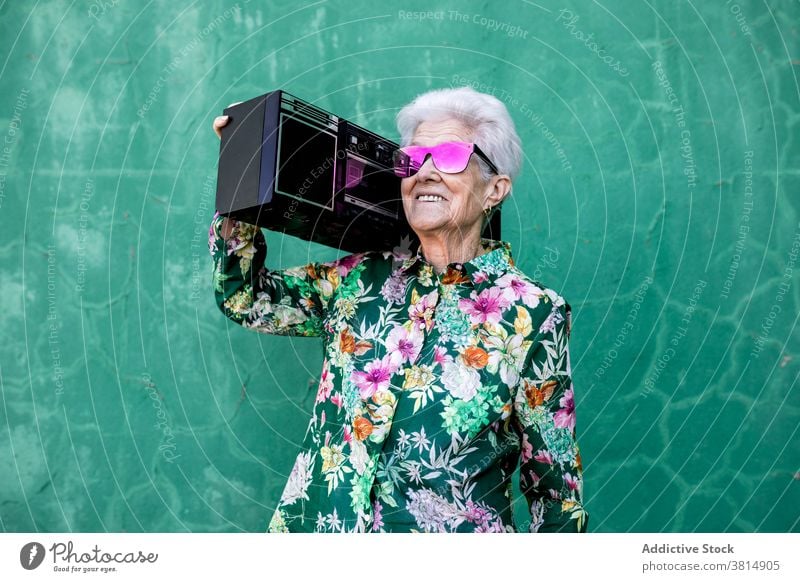 Fröhliche ältere Frau im Hipster-Outfit trägt Plattenspieler Senior trendy Spieler Musik Stil lustig cool farbenfroh Sonnenbrille Mode zuhören urban Lifestyle