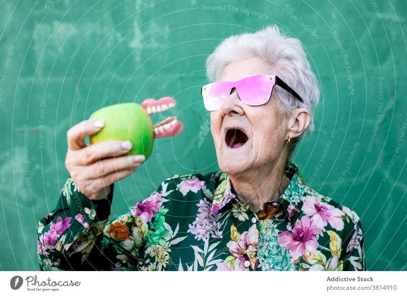 Lustige ältere Frau mit Apfel und Gebiss Senior Zahnersatz Zähne lustig Witz Humor trendy Stil Biss Sonnenbrille Accessoire Dame alt Gesundheitswesen Mund