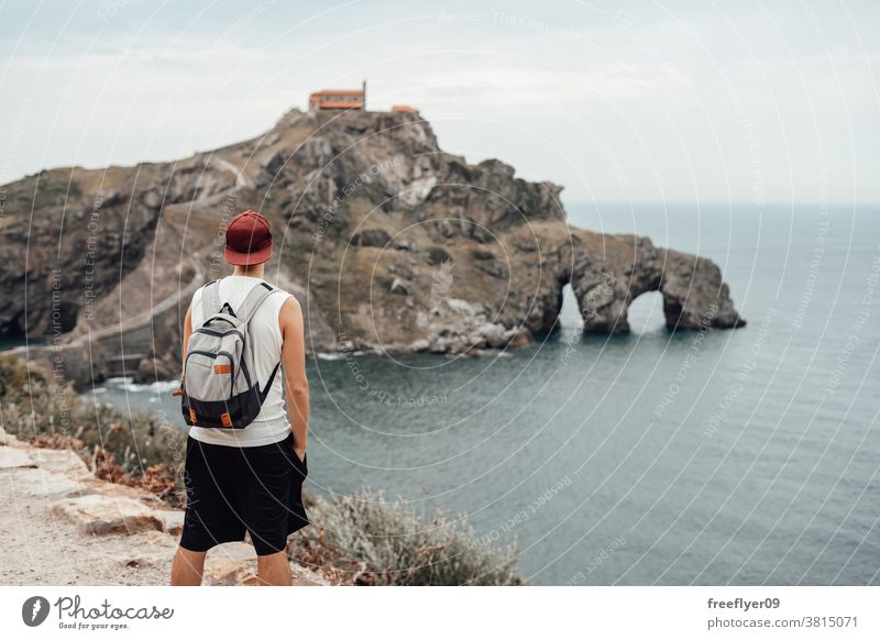 Junger Mann mit Hut vor der Insel Gaztelugatxe eine Tourist Backpacker Rucksack Tourismus Besuch Sightseeing romantisch Vizcaya Spanien Bermeo X Jahrhundert