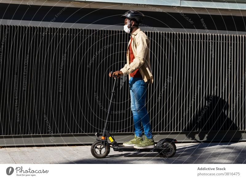 Schwarzer Mann fährt Roller in der Stadt elektrisch Tretroller Mitfahrgelegenheit Großstadt Mundschutz Schutzhelm behüten Coronavirus Fahrzeug männlich ethnisch