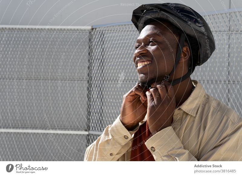 Lächelnder Mann mit Helm auf der Straße Großstadt Schutzhelm angezogen bereit Mitfahrgelegenheit behüten heiter männlich ethnisch schwarz Afroamerikaner Verkehr
