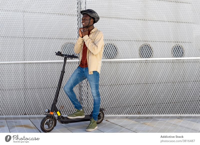 Lächelnder Mann mit Helm in der Nähe von Motorroller auf der Straße elektrisch Tretroller Großstadt Schutzhelm angezogen bereit Mitfahrgelegenheit behüten