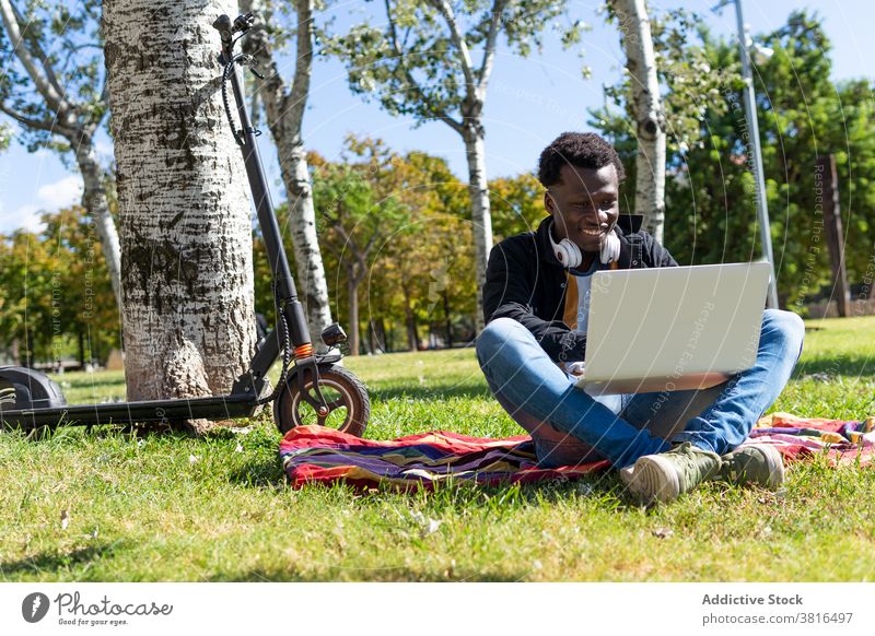 Fröhlicher schwarzer Mann arbeitet am Computer im Park sich[Akk] entspannen Laptop Sommer Tretroller Hipster jung Gerät Wochenende männlich ethnisch