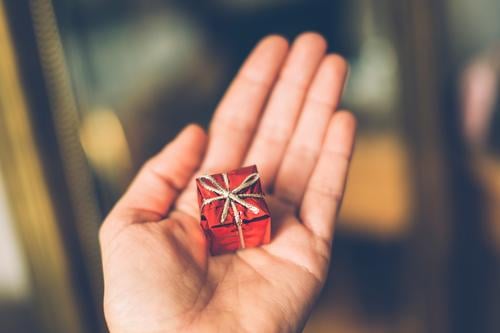 Hand hält ein kleines rotes Geschenk zum Geburtstag oder Weihnachten. verpackt Überraschung Schleife Weihnachtsgeschenk geben schenken Gabe