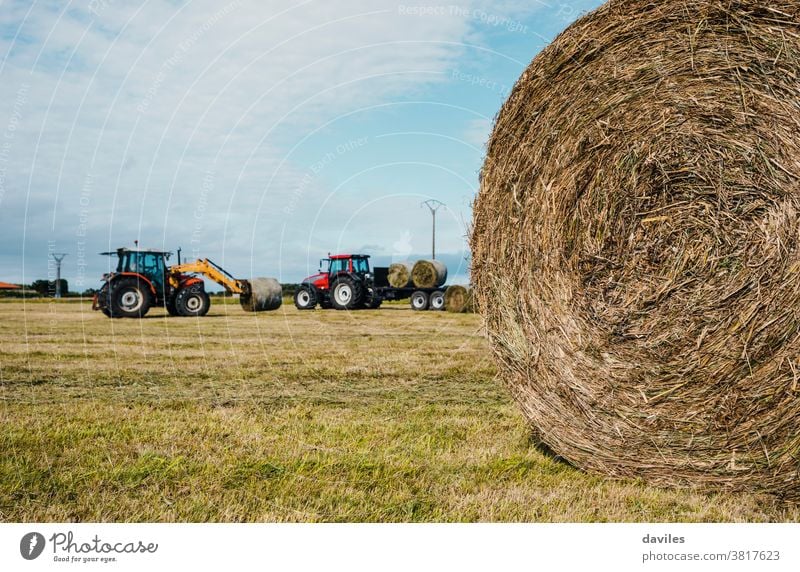 Strohrundballen und zwei im Hintergrund arbeitende Traktoren Erntekampagne Paket Grasland Landschaft Fahrzeug Maschine Verdichter Haufen landwirtschaftlich