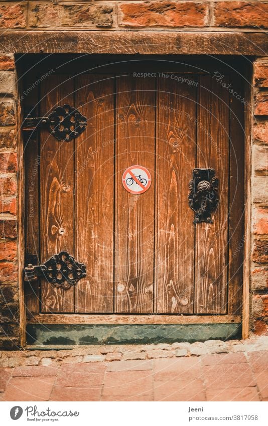 Kleine niedliche Holztür mit alten verzierten Metallbeschlägen - auf der Tür ein Verbotsschild "Fahrräder abstellen verboten" klein Backstein Türbeschlag Wand