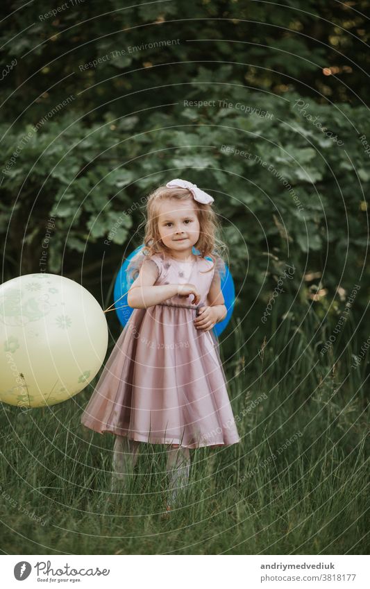 Stylisches Mädchen im Alter von 4-5 Jahren hält einen großen Ballon in der Hand und trägt ein trendiges rosa Kleid auf der Wiese. Verspieltes. kleines Mädchen mit einem Ballon im Park. Geburtstagsfeier.