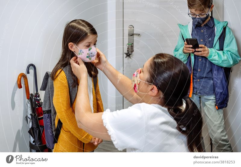Mutter setzt ihrer Tochter die Maske auf vorbereitend Gesichtsmaske zur Schule gehen covid-19 Coronavirus Schutzmaske korrekt passende Maske