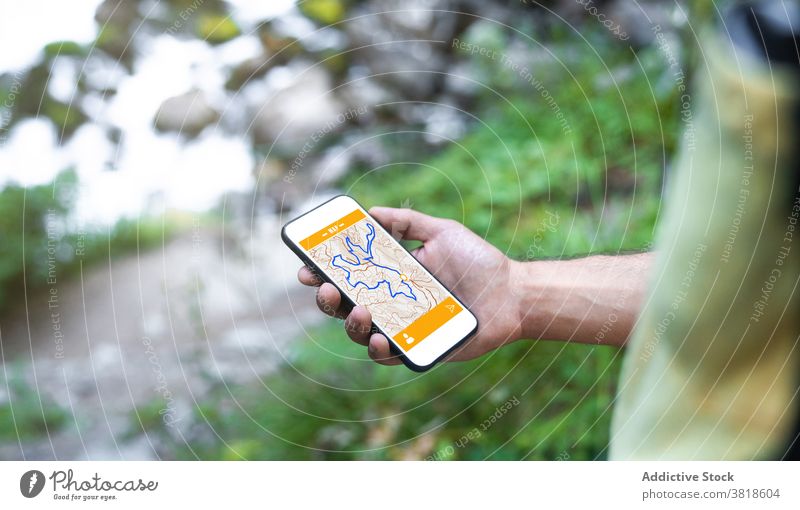 Anonymes Männchen, das im Wald steht und eine Kartenanwendung auf dem Mobiltelefon aufnimmt Mann Reisender Smartphone Bach Berghang Uelhs deth Joeu Fluss Handy