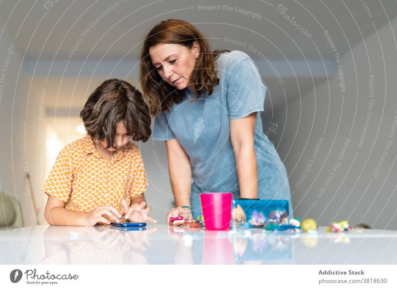 Mutter und anonymer Sohn chatten auf Smartphone zu Hause Internet Kinderbetreuung Mutterschaft Zeit verbringen Kindheit Spielzeug benutzend Apparatur Surfen