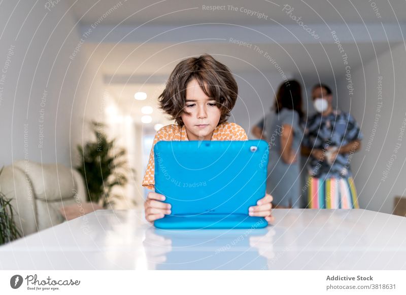 Fokussierter Junge, der zu Hause hinter nicht erkennbaren Eltern auf den Laptop schaut zuschauend Internet online Kindheit Tisch heimwärts benutzend Apparatur