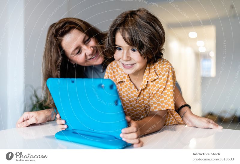 Aufgeregter Junge mit Laptop in der Nähe von lächelnden Mutter zu Hause aufgeregt Kindheit Mutterschaft freie Zeit Wochenende heimwärts benutzend Apparatur
