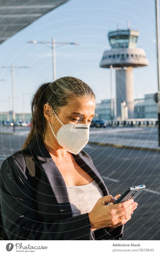 Frau in Maske wartet auf Taxi im Flughafen Browsen warten ankommen Coronavirus Mundschutz behüten Seuche Reisender Smartphone Koffer Gepäck Atemschutzgerät