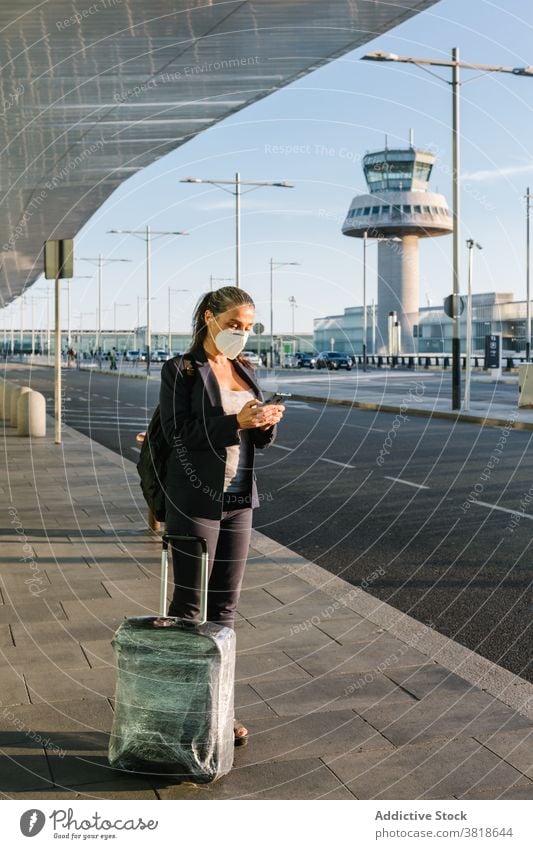 Frau in Maske wartet auf Taxi im Flughafen Browsen warten ankommen Coronavirus Mundschutz behüten Seuche Reisender Smartphone Koffer Gepäck Atemschutzgerät