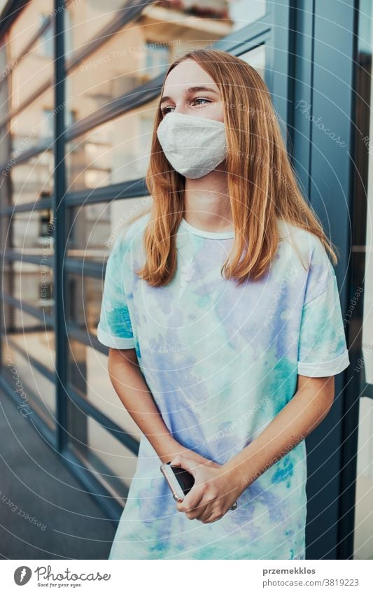 Porträt einer jungen Frau, die an der Ladenfront in der Innenstadt steht und eine Gesichtsmaske trägt, um eine Virusinfektion zu vermeiden Kaukasier Funktelefon