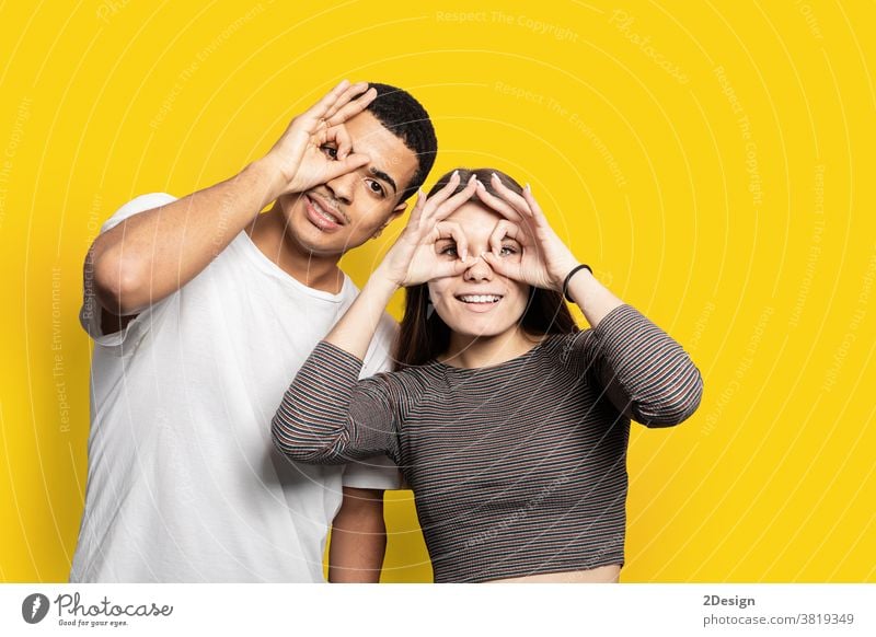 Porträt eines fröhlichen, fröhlichen Paares beim Fernglasbau mit Fingern in lässigen Hemden, isoliert auf leuchtend gelbem Hintergrund sich[Akk] entspannen 2