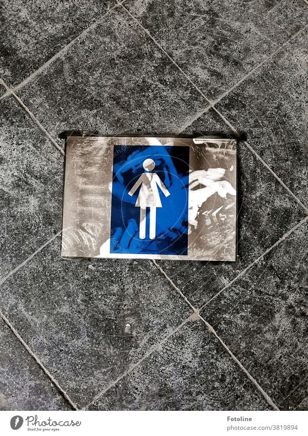 In einem Lost Place liegt das Schild für die Damentoilette verschmutzt auf dem Boden. Hinweisschild schmutzig lost places alt Menschenleer Farbfoto Tag