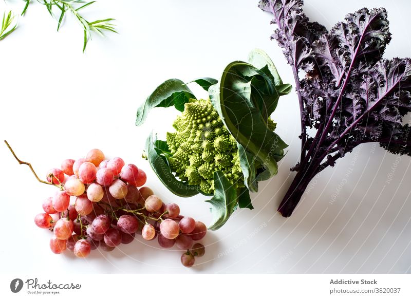 Flatlay mit lila Grünkohl, rosa Weintrauben und Romanesco-Kohl Lebensmittel Frucht Gemüse Kraut sortiert produzieren Vegetarier flache Verlegung Draufsicht weiß