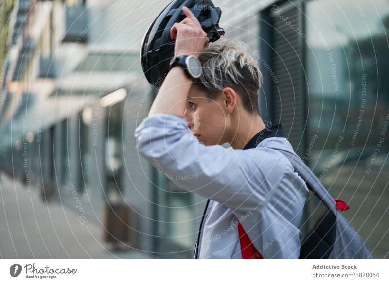 Junge Frau Radfahrer setzt auf Helm, während stehend neben modernen Gebäude auf Sommertag in der Stadt Schutzhelm legt an Nahaufnahme Seitenansicht Fahrrad