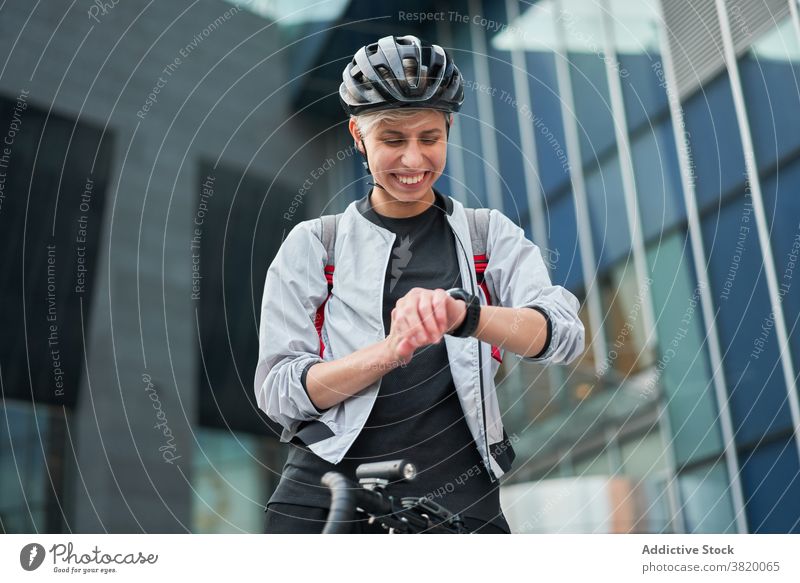 Junge Frau Radfahrer schaut auf Armbanduhr auf dem Hintergrund der modernen Gebäude Großstadt Tag jung Sport Reiten Sommer Schutzhelm schützend Glück Mädchen